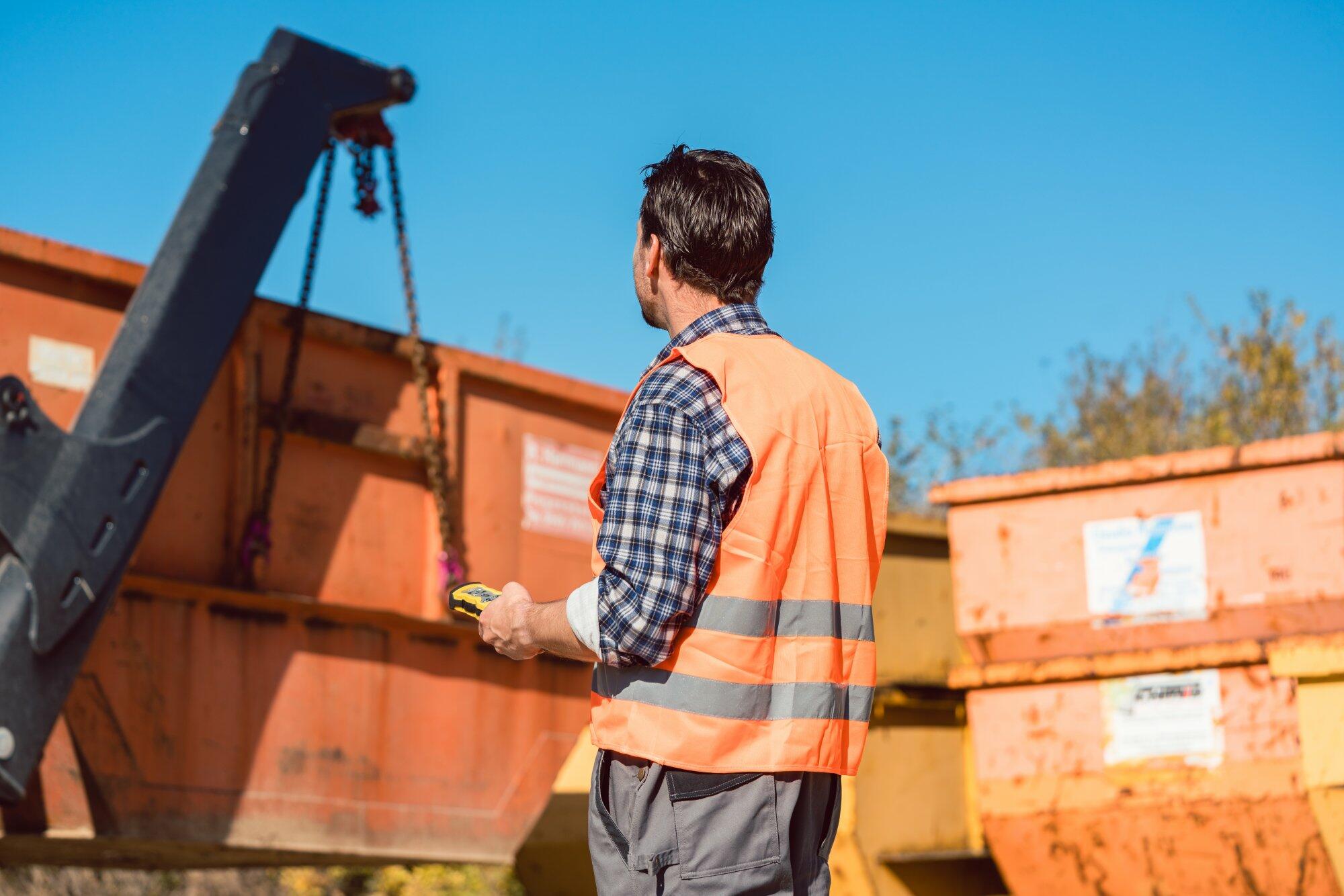 Arbeiter mit Warnweste bedient Kran neben Container